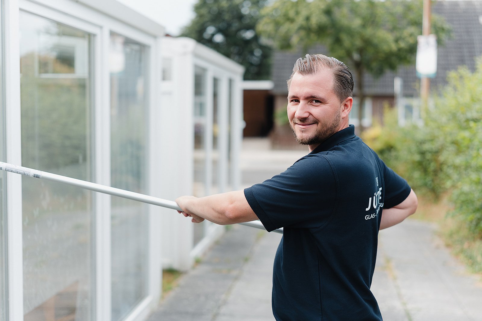 Florian Jüttner bei der Fensterreinigung mit Teleskopstange, lächelnd in die Kamera schauend