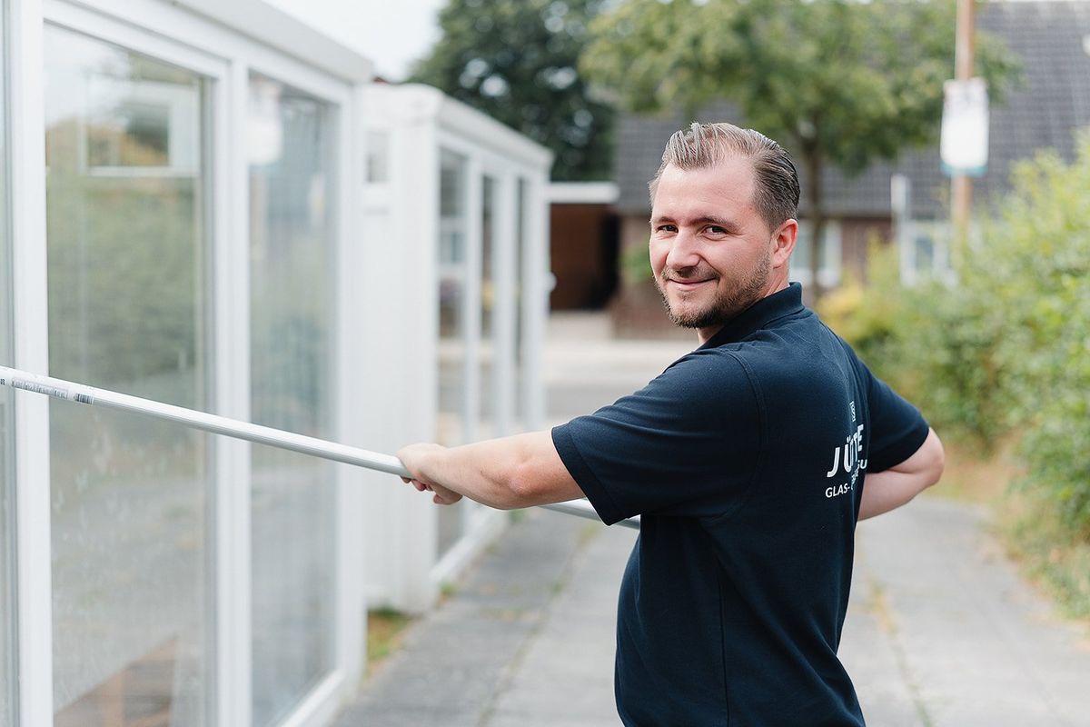 Florian Jüttner bei der Fensterreinigung mit Teleskopstange, lächelnd in die Kamera schauend